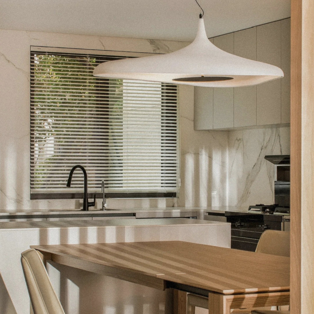 white modern pendant light hanging above a kitchen dining table in a bright contemporary home interior.