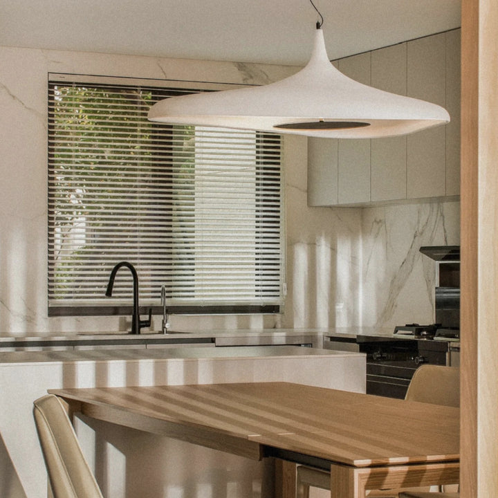 white modern pendant light hanging above a kitchen dining table in a bright contemporary home interior.