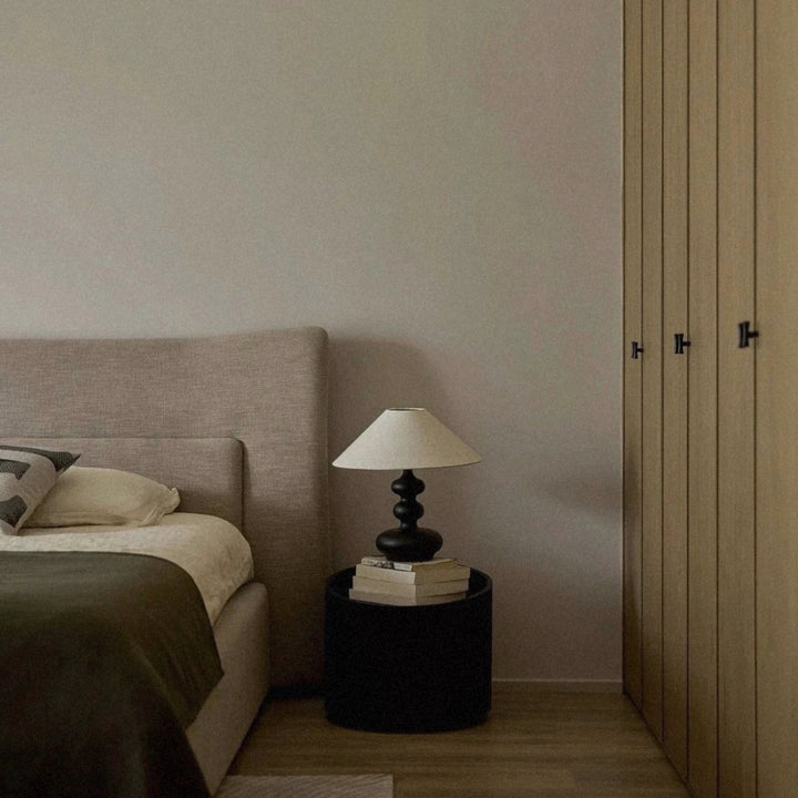 wood table lamp placed beside a bed in a modern neutral bedroom.