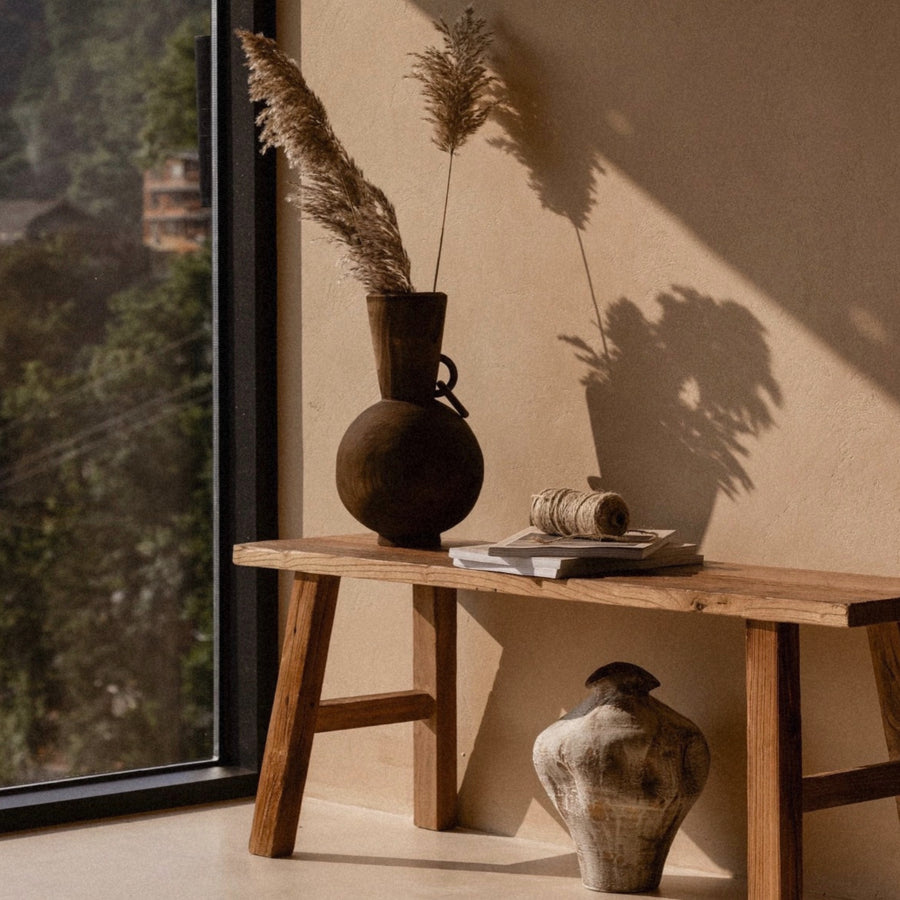 wood vase with dried branches styled on a console table in a warm natural interior.