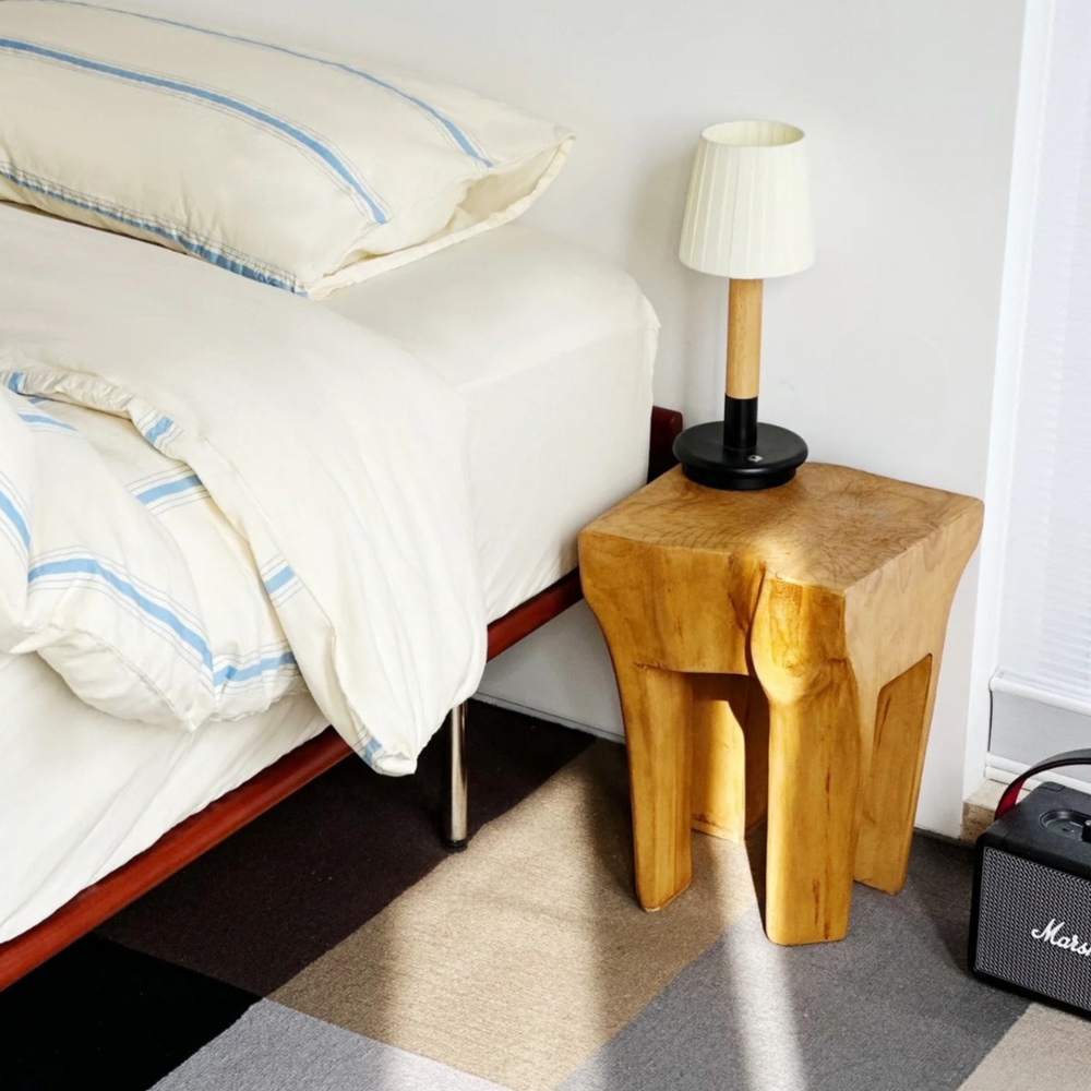 Bedroom scene showing a cordless lamp on a wooden nightstand next to a bed with blue-striped bedding, offering a warm, inviting glow.